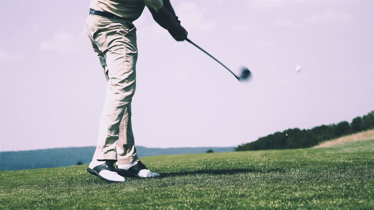 Golfer following through on a tee shot on a green course, seen from the shoulders down